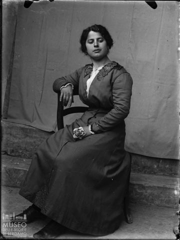 Piazza Brembana. Ritratto di donna seduta con fiore in mano