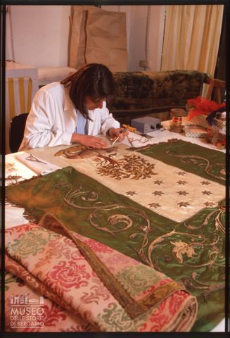 Ragazza al lavoro su un antico stendardo a Siena