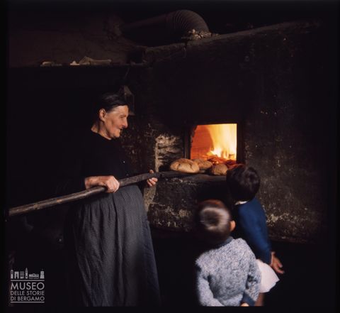Una donna che sforna pani in un antico forno di Corteno Golgi