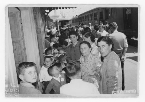 Gruppo di bambini accompagnati da adulti ritratti in una stazione
