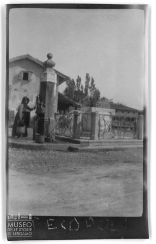 Ritratto di una donna che riempie dei secchi di acqua alla fontana