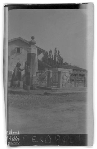 Ritratto di una donna che riempie dei secchi di acqua alla fontana